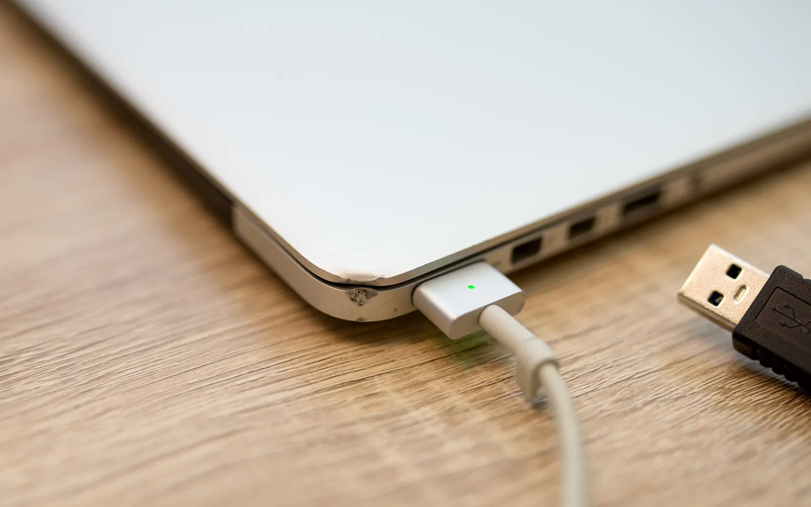 Close-up of a laptop on a wooden table with a USB cable beside its ports