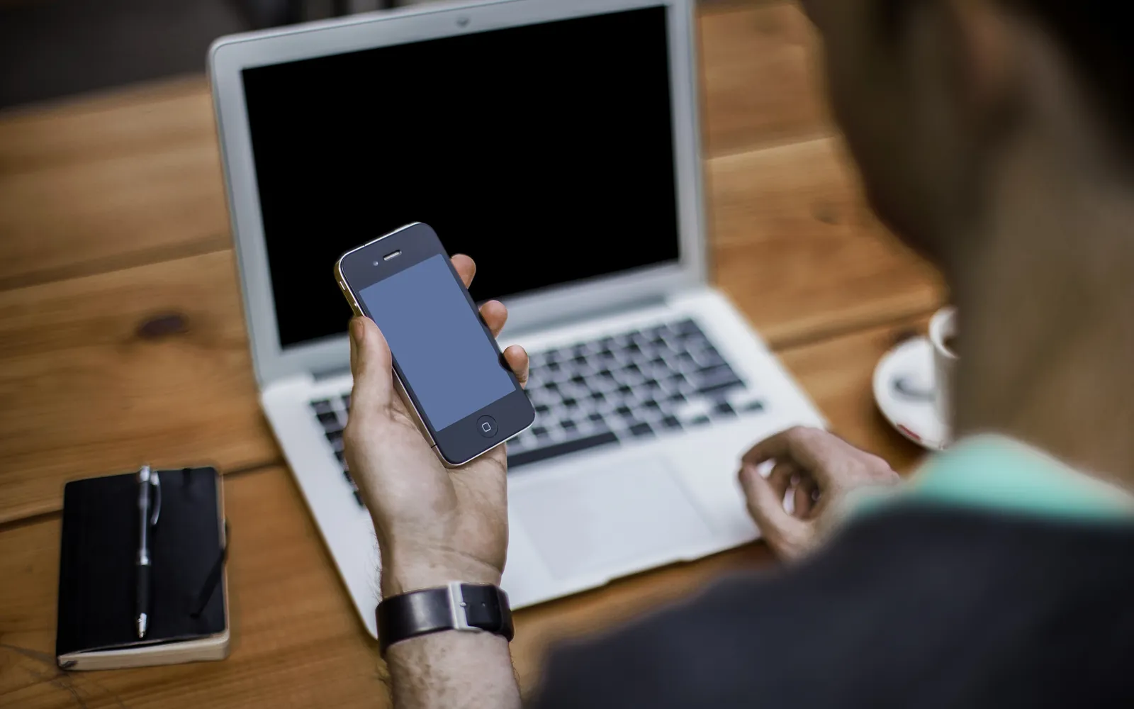 A person holding a smartphone in front of a laptop